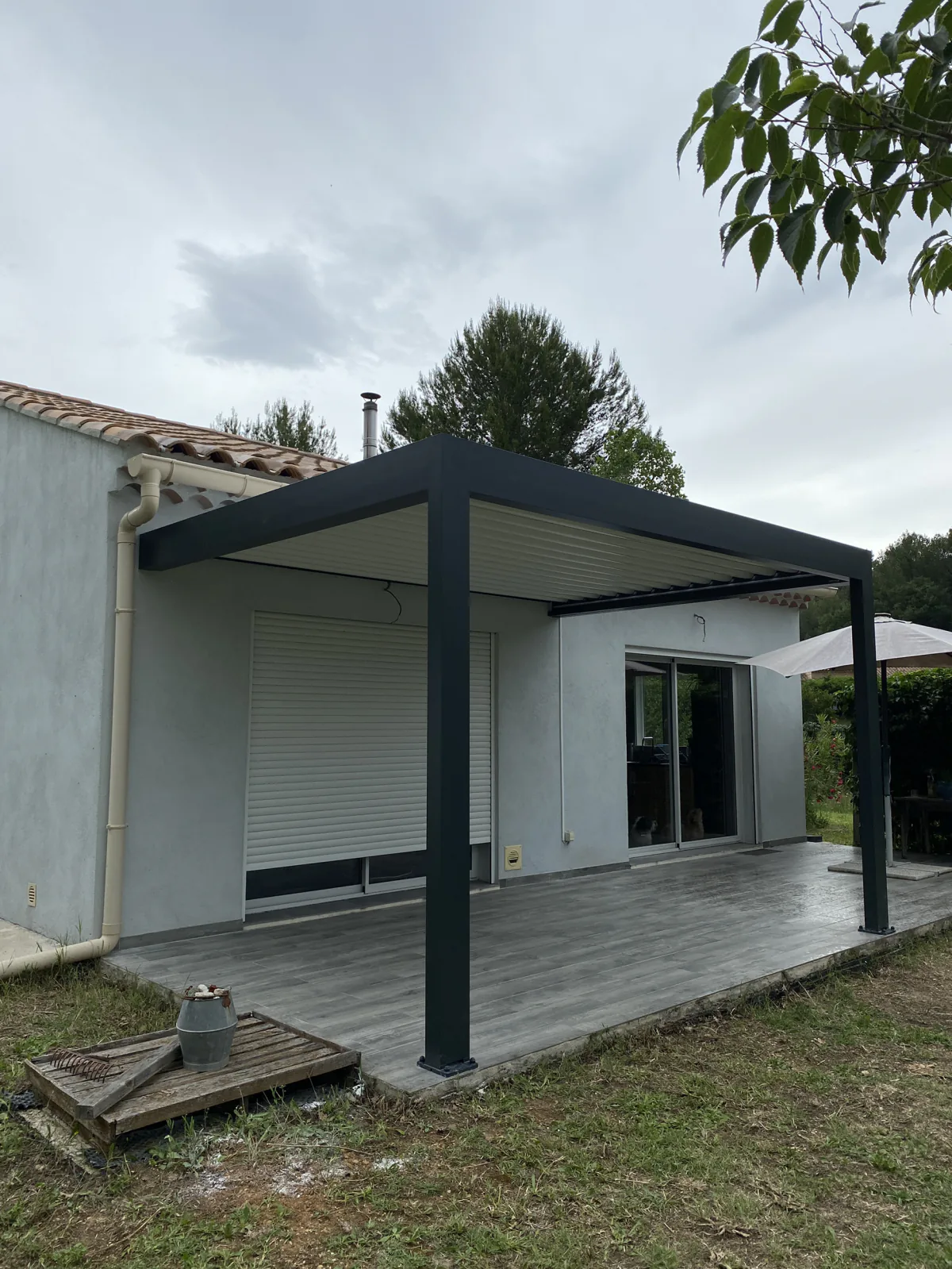 Pergola aluminium anthracite devant une maison équipée de baies vitrées et de volets roulants